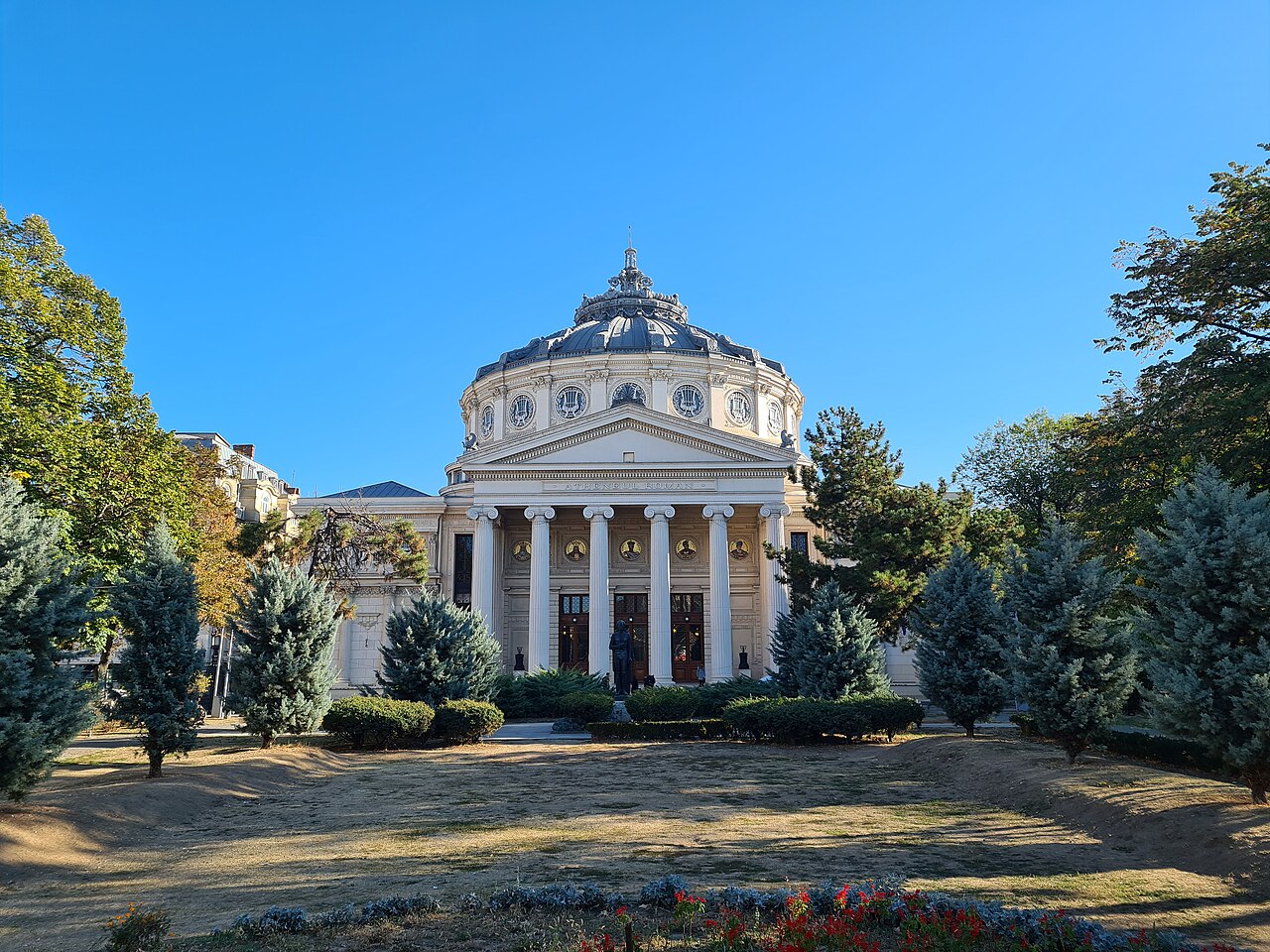 The dome and columned entrance of the Romanian Athenaeum in Bucharest, framed by trees.